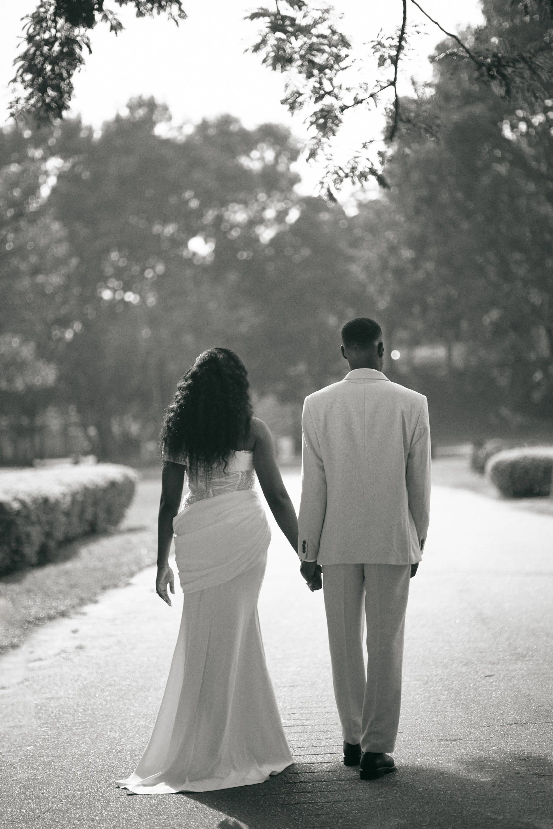 A couple walking hand in hand down a tree-lined path, in black and white